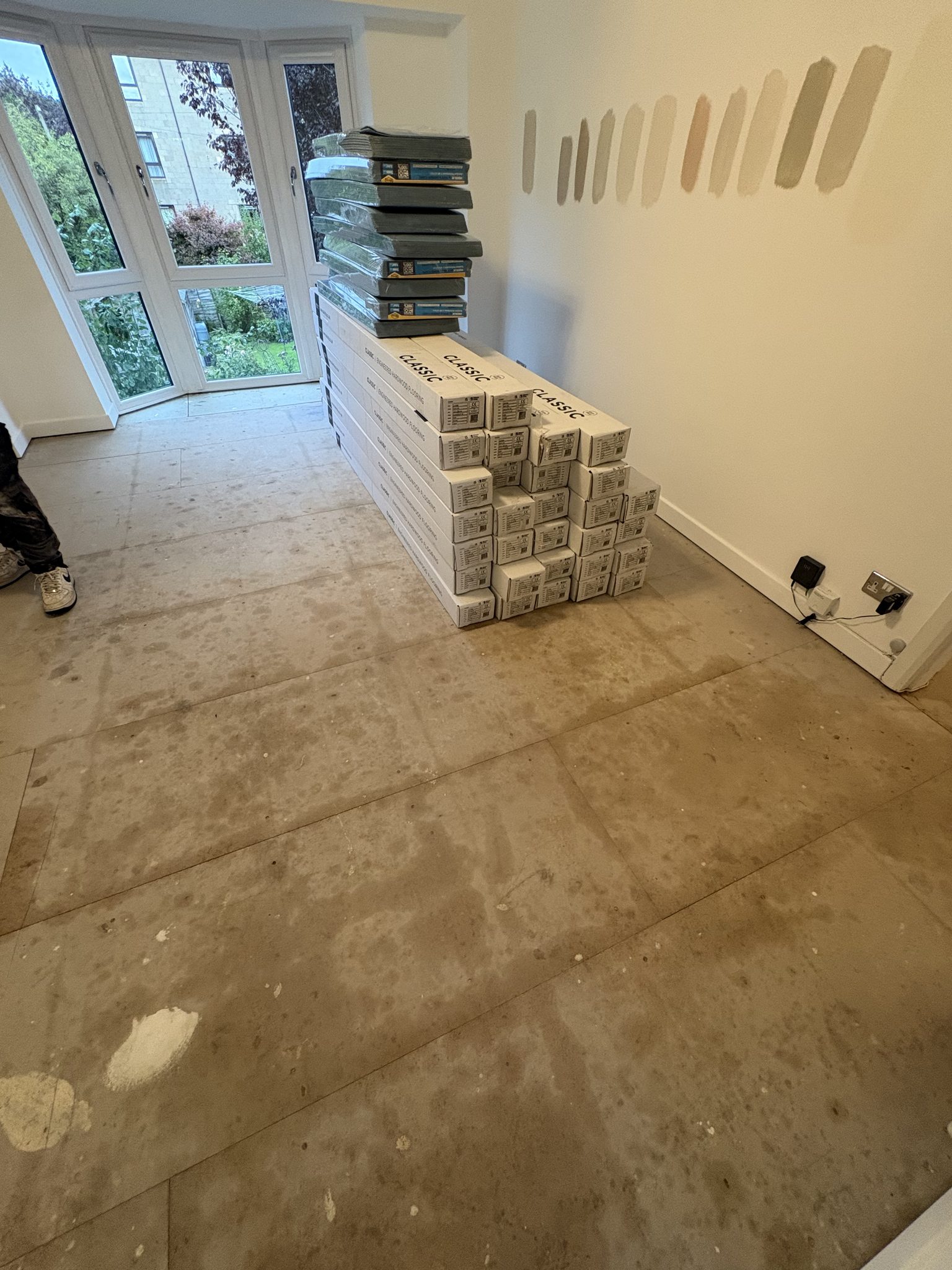 Bay windowed room in Bridge of Allan with the floor boarded out and boxes of engineered hardwood flooring stacked against the wall