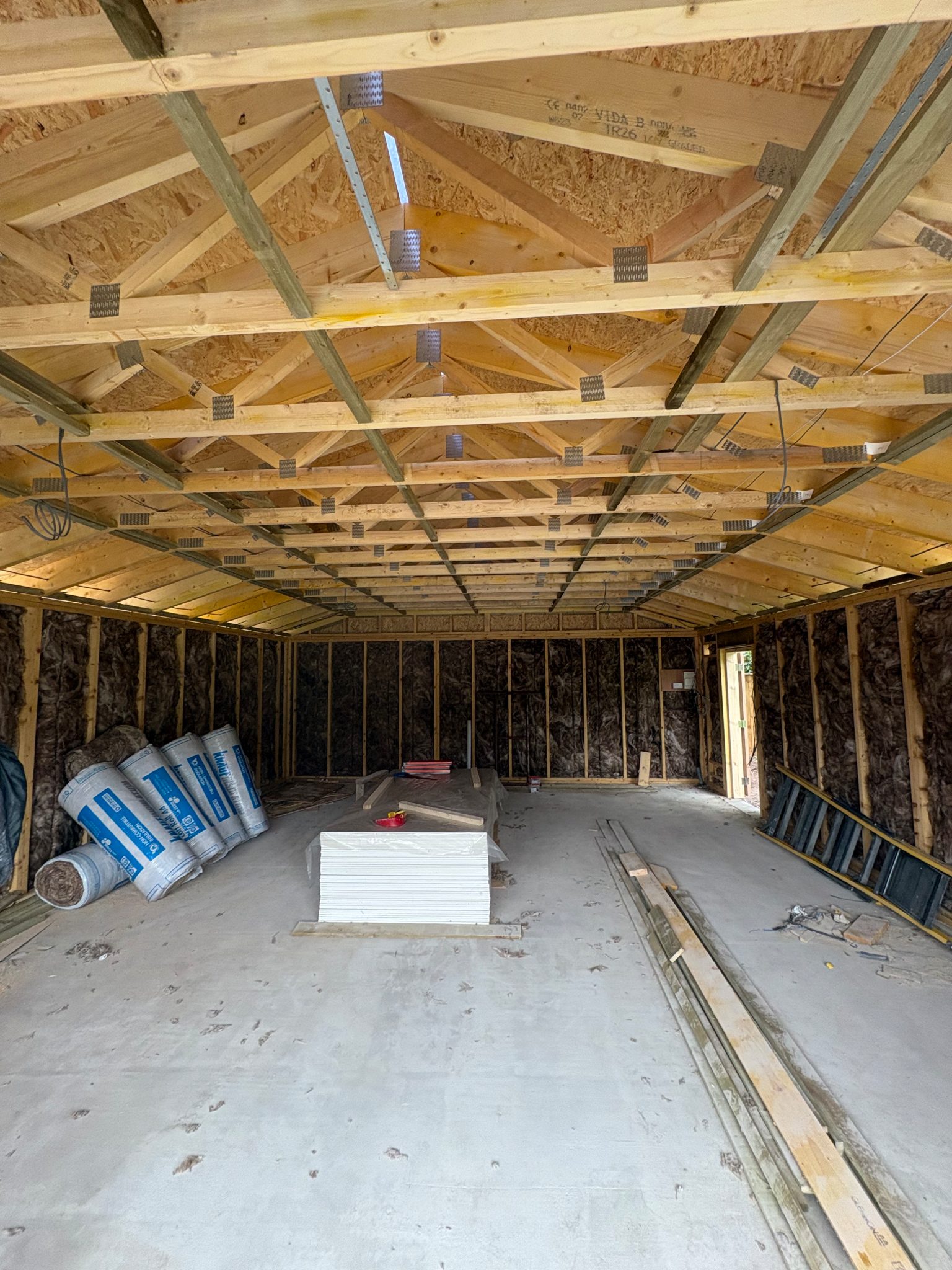 Insulation fitted between the studs and roof timbers of the garage, with plasterboard stacked on the floor